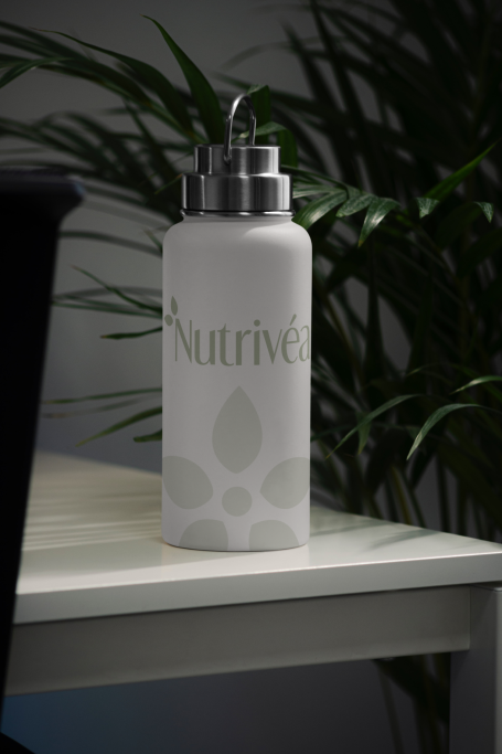 Bouteille blanche avec inscription "Nutriv" sur un bureau, en arrière-plan de plantes.