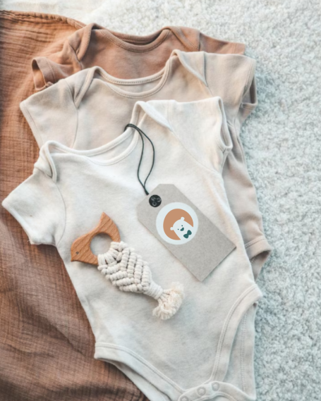 Trois bodies de bébé beige avec une étiquette et un jouet en forme de poisson.