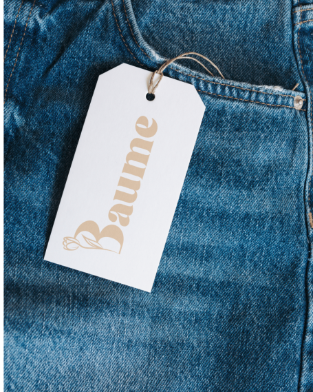 Étiquette blanche portant le mot "Baume" accrochée à un jean en denim.