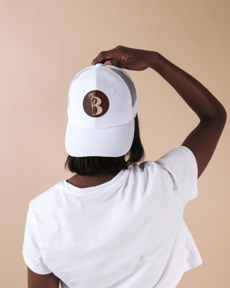 Person de dos portant une casquette blanche avec un logo rond marron, sur fond neutre.