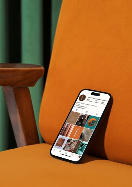 Un smartphone posé sur un fauteuil orange avec un fond de rideaux verts.
