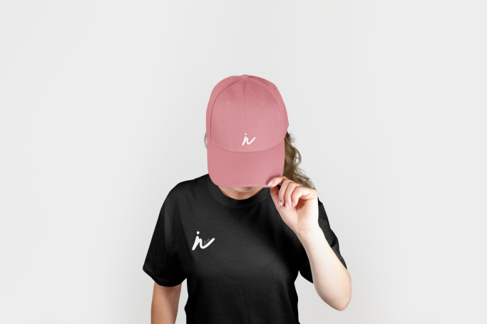 Person en t-shirt noir portant une casquette rose, la tête légèrement inclinée.
