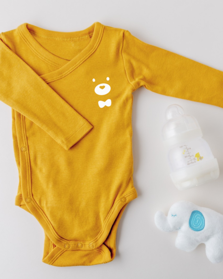 Body en cotton jaune avec motif ours, accompagné d'une bouteille et d'un jouet éléphant.